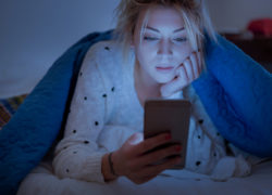 Disappointed sad woman holding mobile phone while laying on bed at night